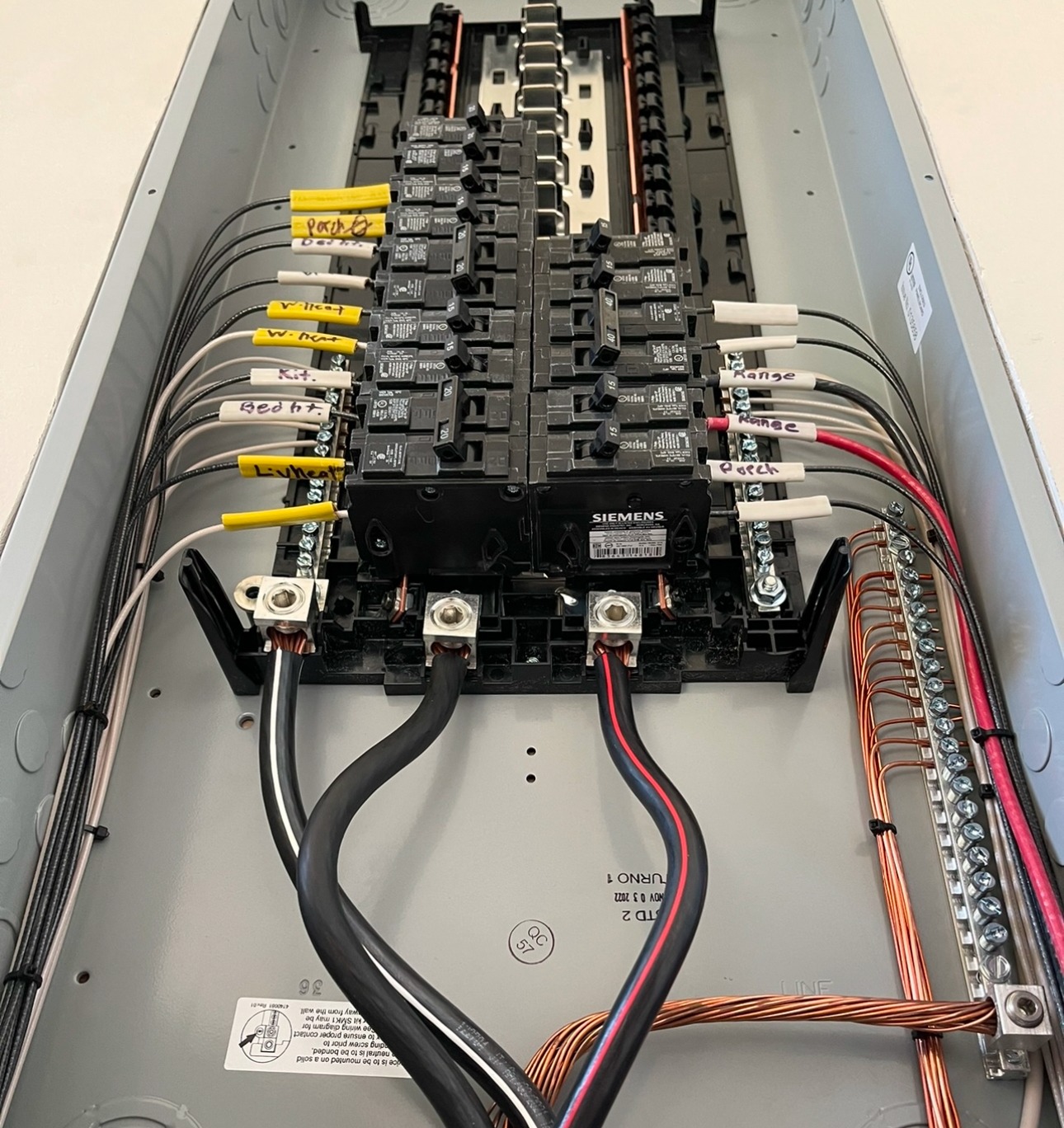 Interior electrical panel showing labeled circuit conductors, breakers and organized wire routing, photographed with its cover removed.